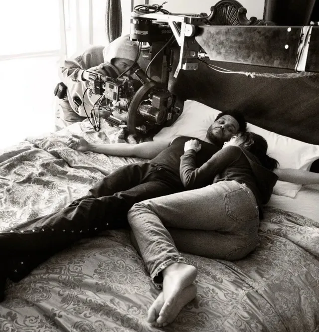 Jenna Ortega reclining on a bed in a black and white behind the scenes photograph.
