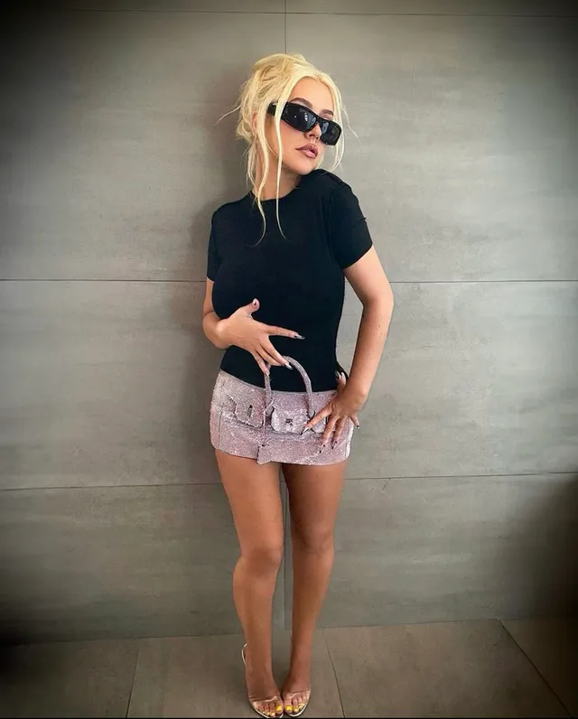 Christina Aguilera posing in a black top, pale skirt and clear heels.