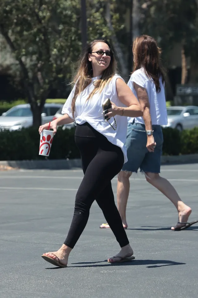Kaley Cuoco walking in black leggings and flip-flops.