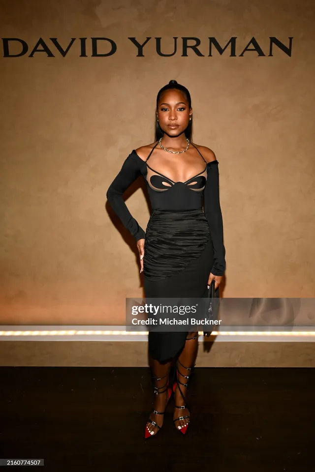 Carlacia Grant posing in a black dress and lace-up heels at an event.