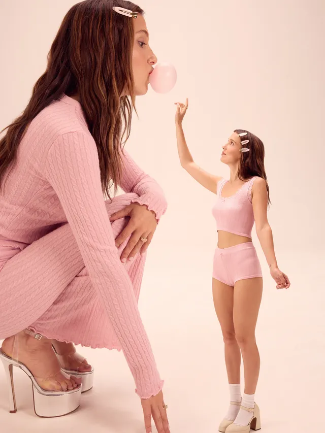 Millie Bobby Brown: posing in a pink outfit and platform heels in a studio composition.