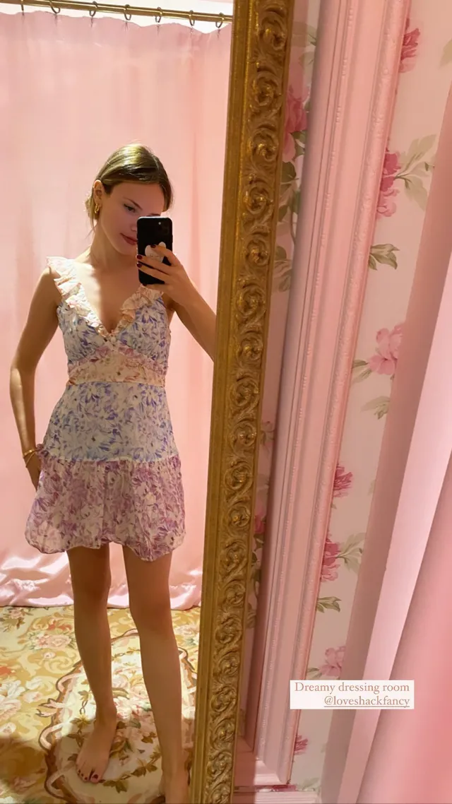 Halston Sage taking a mirror selfie in a pale floral mini dress and heels.