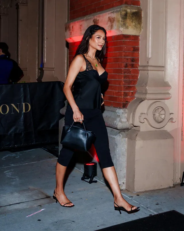 Shay Mitchell walking outside in a black satin dress and heels.