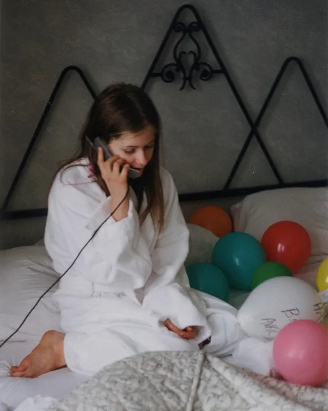 Avril Lavigne sitting barefoot on a bed in a white robe.