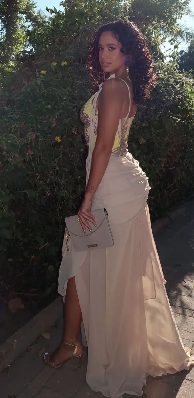 Emily Tosta posing in a pale gown and heels.