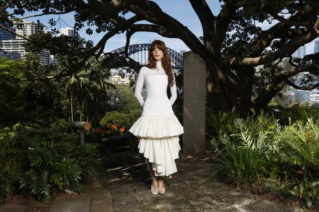 Daisy Edgar-Jones standing in a garden wearing a white dress and heels.