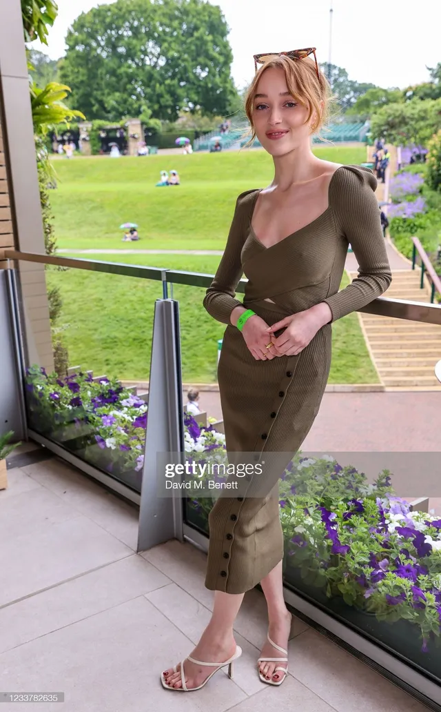 Phoebe Dynevor posing outdoors in an olive dress and pale heels.