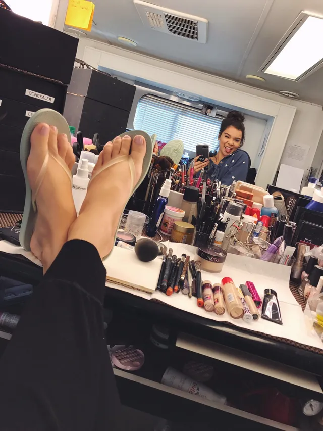 Hailee Steinfeld resting bare feet beside a makeup mirror.