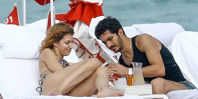 Úrsula Corberó sitting barefoot beside a man on a beach lounger.