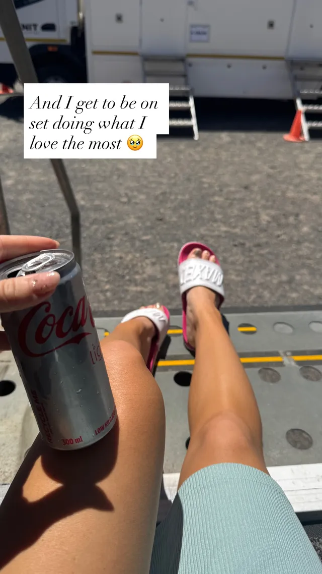 Brec Bassinger shown reclining outdoors in a pale outfit and white slides.