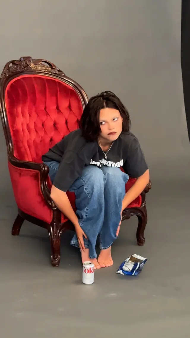 Ariana Greenblatt sitting in a red chair while handling a casual shoe.