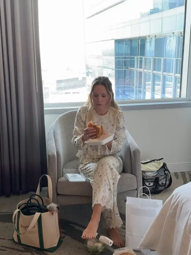 Kristen Bell sitting barefoot by a window in patterned pajamas.