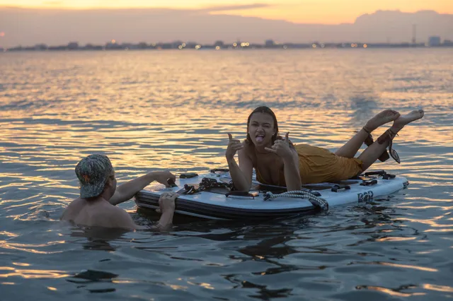 Madison Bailey lying barefoot on a paddleboard at sunset.