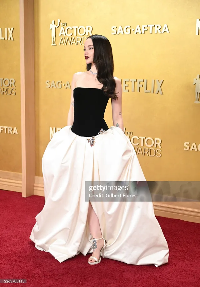 Dove Cameron wearing a black-and-white gown with metallic heels.