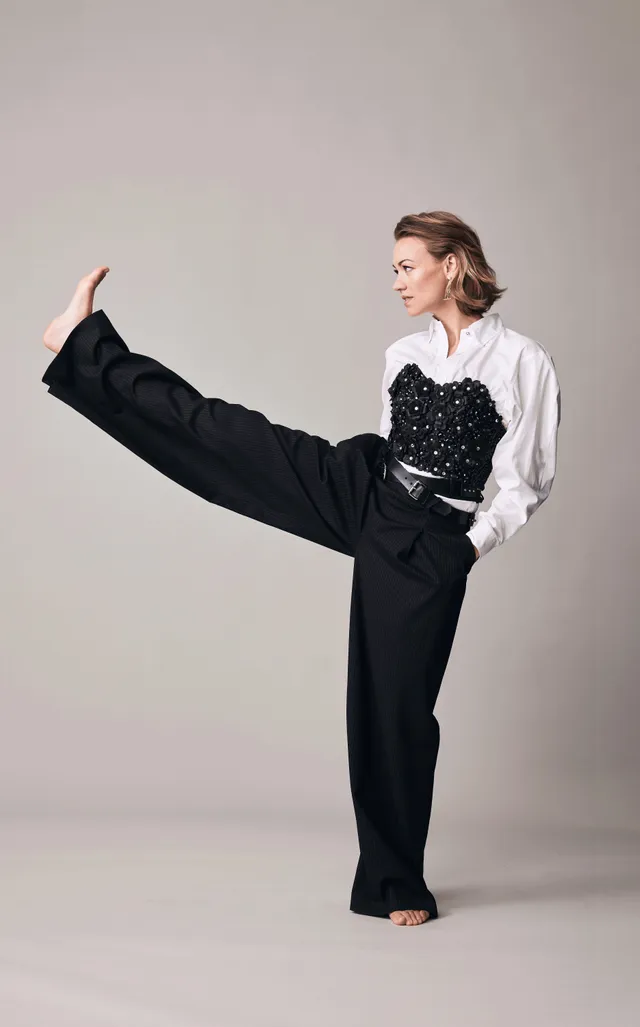 Yvonne Strahovski posing for a studio portrait in wide-leg trousers.