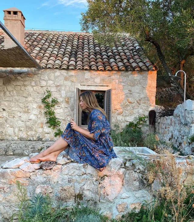 Maria Sharapova sitting barefoot on a stone wall in a blue patterned dress.