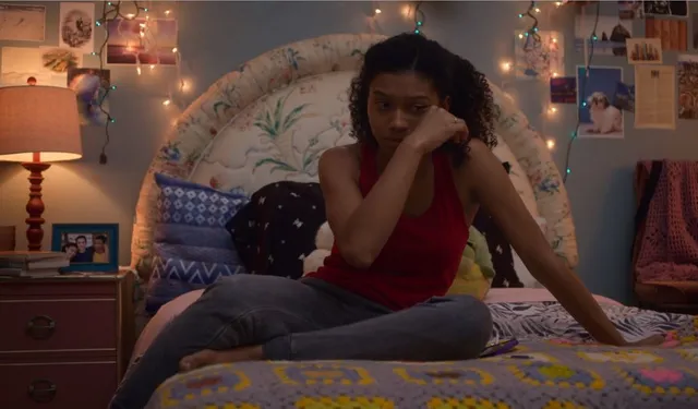 Sierra Capri sitting cross-legged on a bed in a red top and jeans.