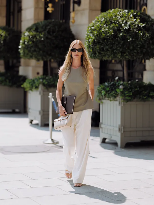 Rosie Huntington-Whiteley walking outdoors in white trousers and pale heels.