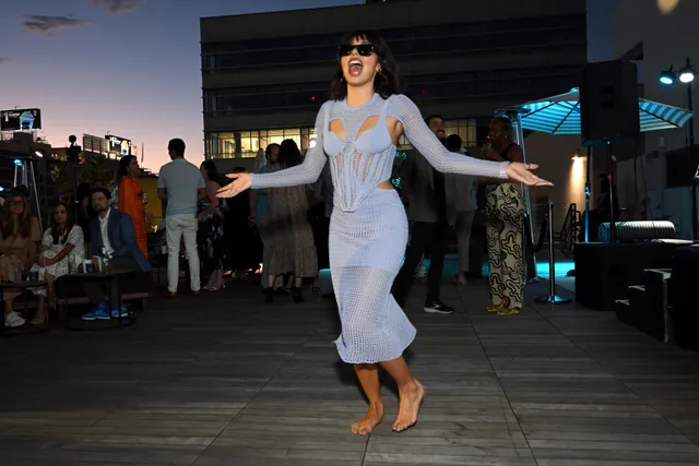 Xochitl Gomez walking barefoot outdoors at dusk in a lavender dress.