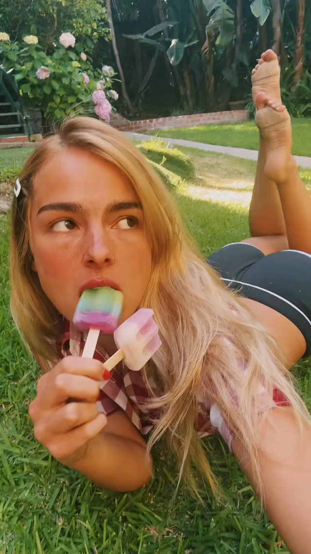 Addison Rae lying on grass with a bare foot raised.
