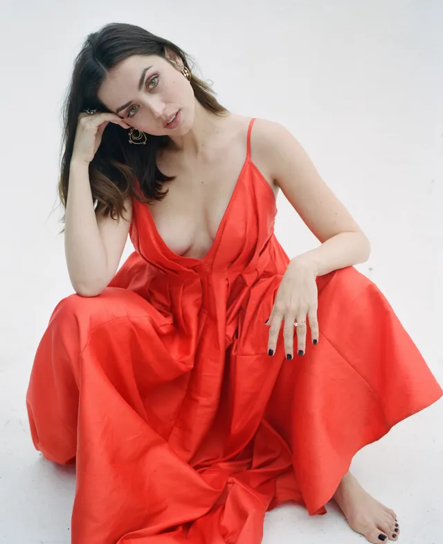 Ana de Armas: seated barefoot in a red dress against a light background.