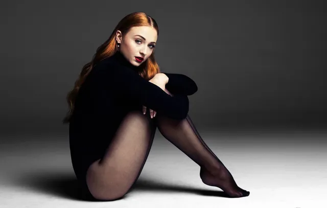 Sophie Turner a seated black outfit with sheer tights.