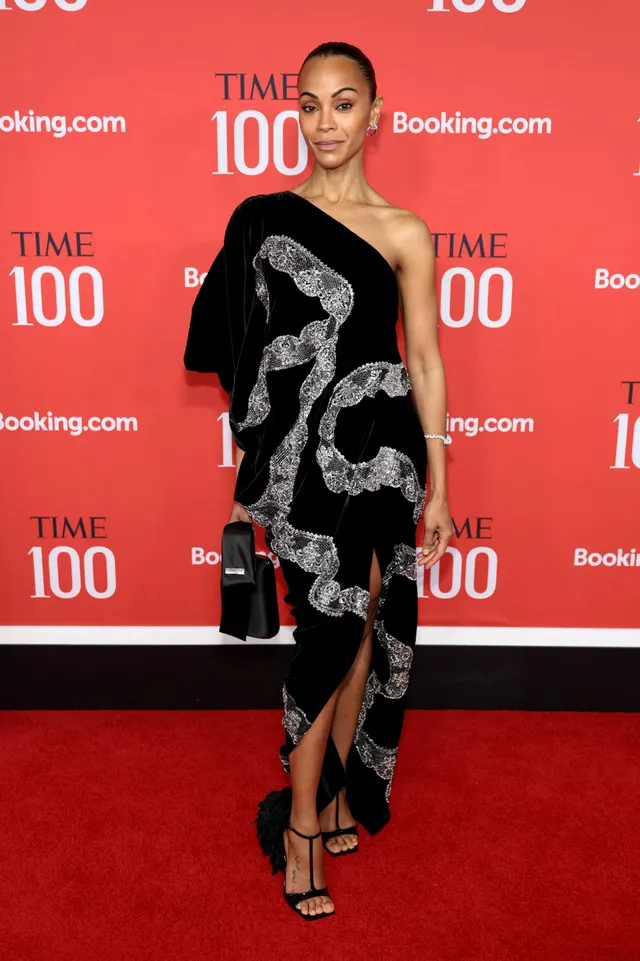 Zoe Saldaña posing on a red carpet in a black patterned gown.