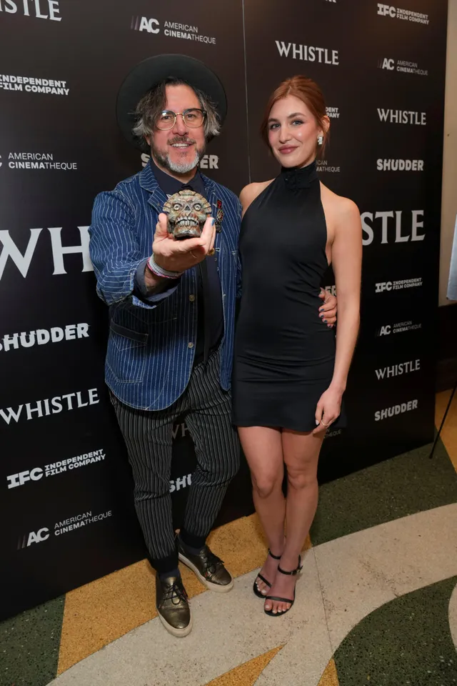 Sophie Nélisse posing beside a man in a black dress and black heels.