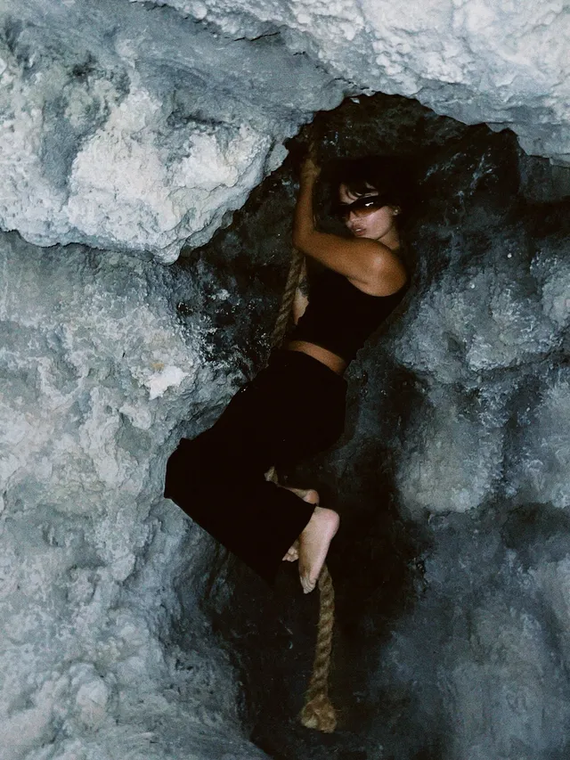 Isabela Merced holding a rope while barefoot against a rock wall.