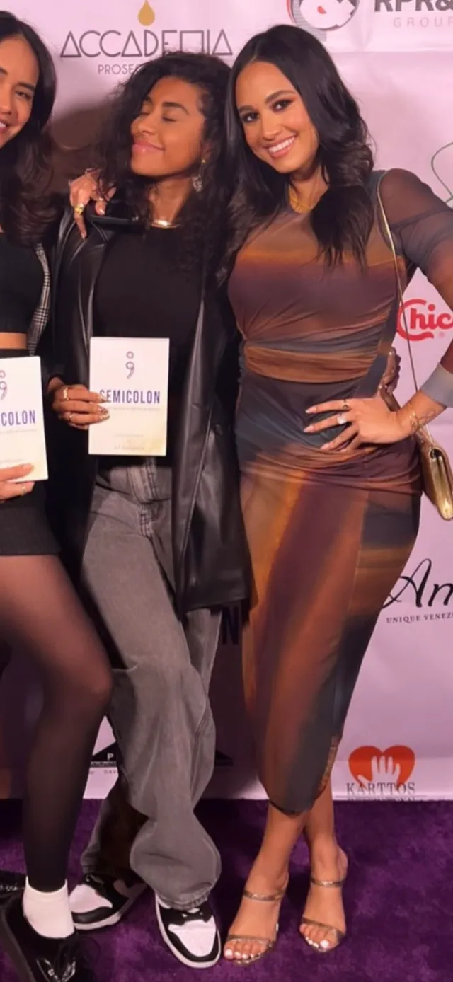 Emily Tosta posing with guests in a brown dress and heels.