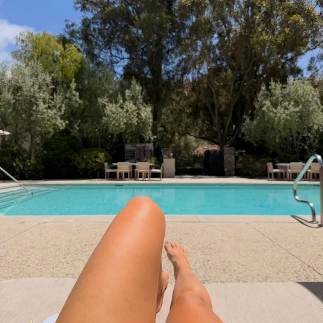 Ashley Tisdale relaxing barefoot on a lounger beside a swimming pool.