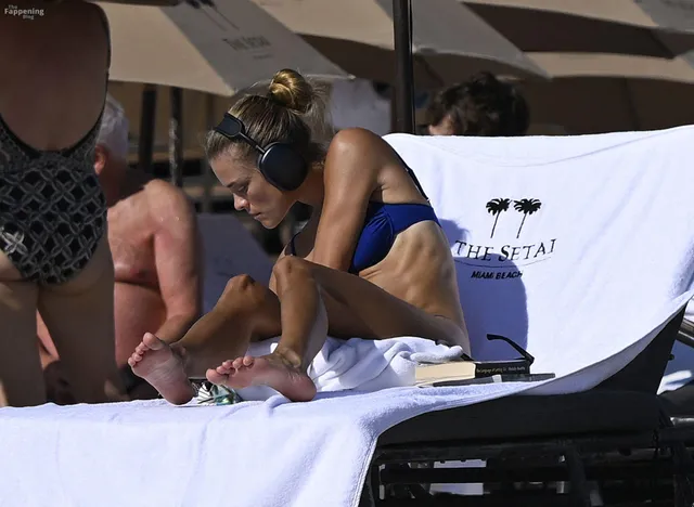 Nina Agdal sitting barefoot on a lounger while eating.