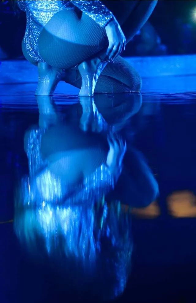 Beyoncé crouching in a stage costume and high heels under blue light.