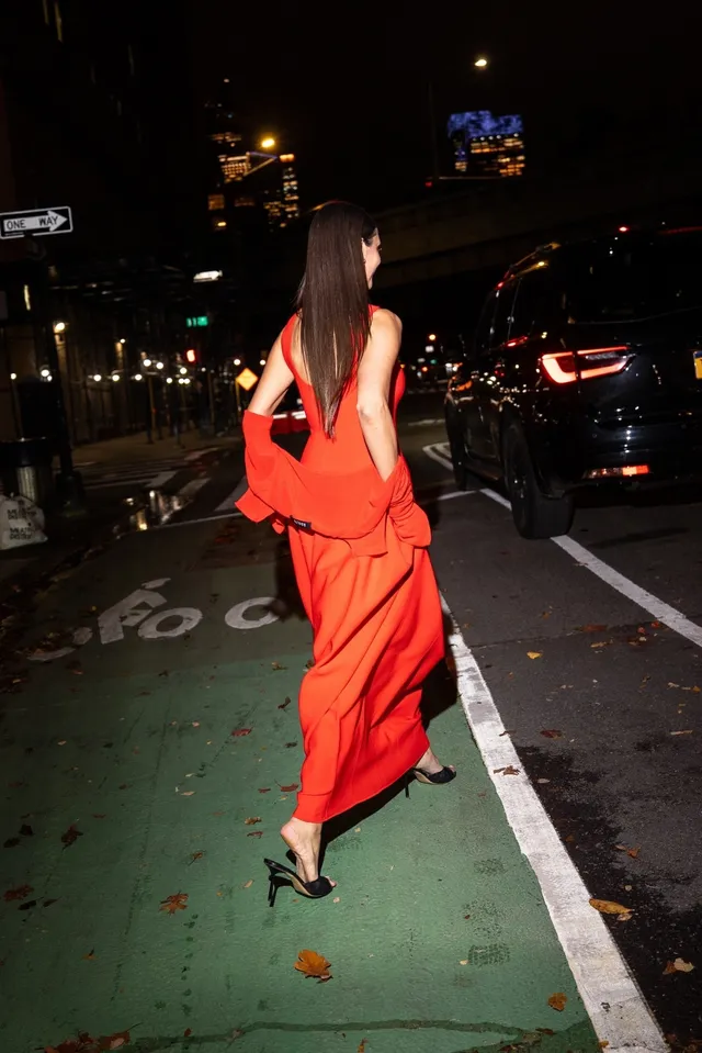 Nina Dobrev walking outdoors in a red dress and black heels.