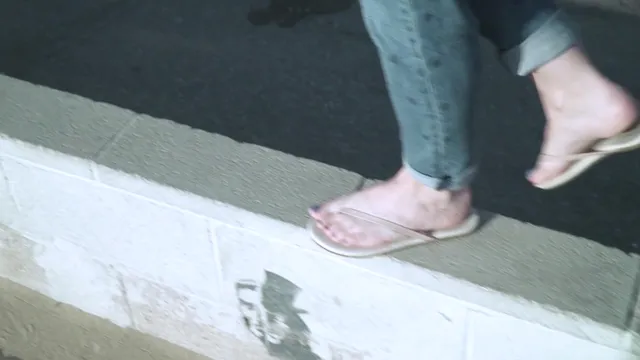 Elisha Cuthbert walking in pale flip-flops beside a pavement.