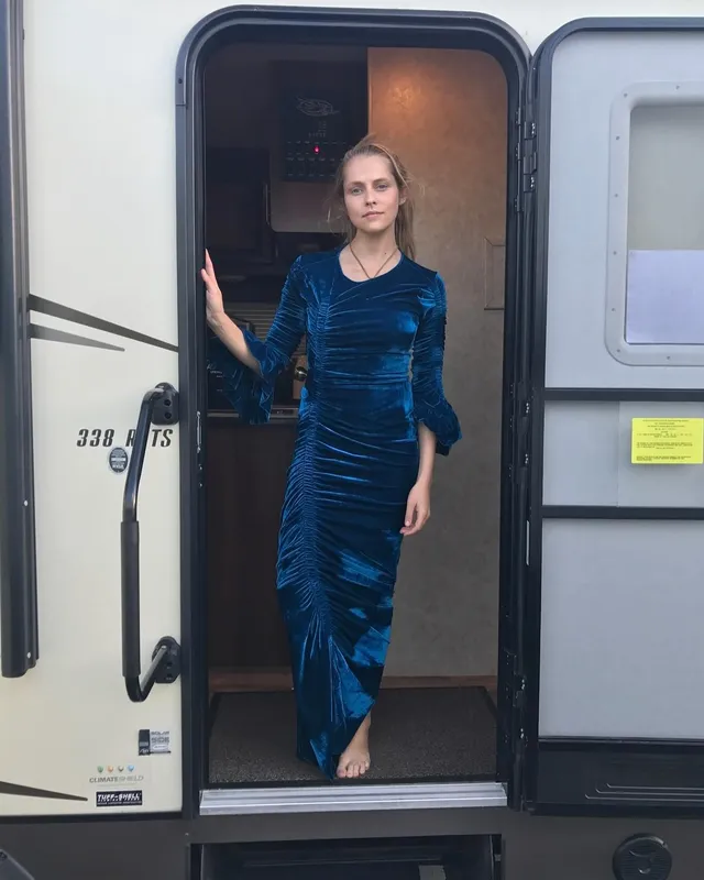 Teresa Palmer standing in a trailer doorway in a blue dress.