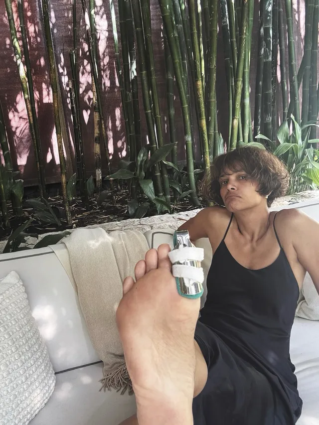 Halle Berry reclining barefoot on an outdoor sofa in a black outfit.