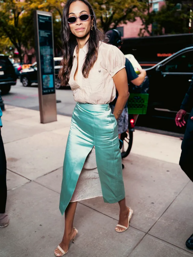 Zoe Saldaña posing outside a vehicle in a turquoise skirt.