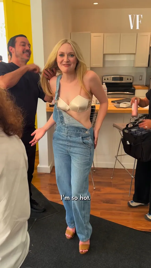 Dakota Fanning standing indoors in jeans and a light top.