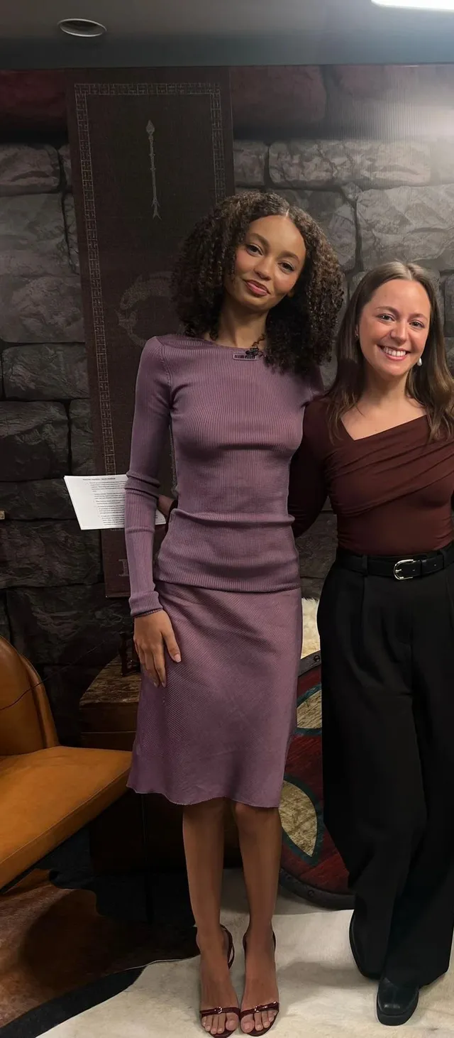 Nico Parker standing beside a friend in a purple dress and heels.