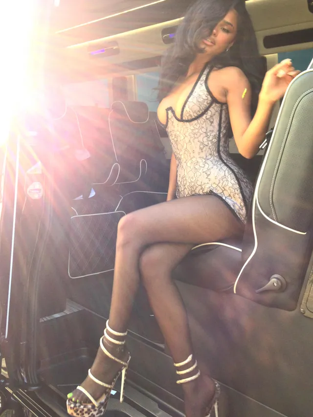 Tyla sitting in strappy heels and a silver-and-black outfit indoors.