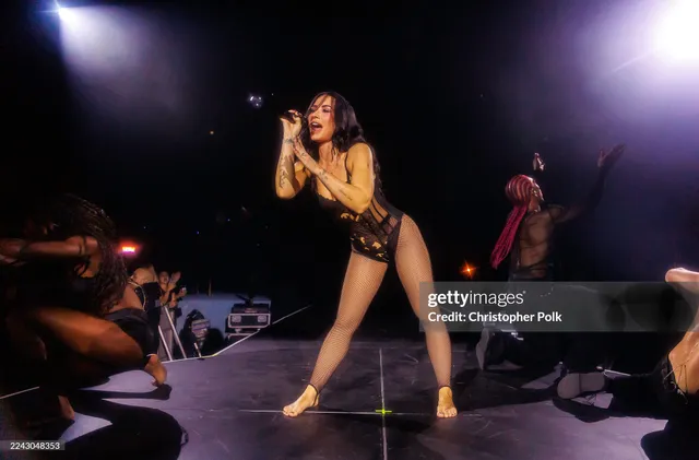 Demi Lovato singing on stage in gold heels.