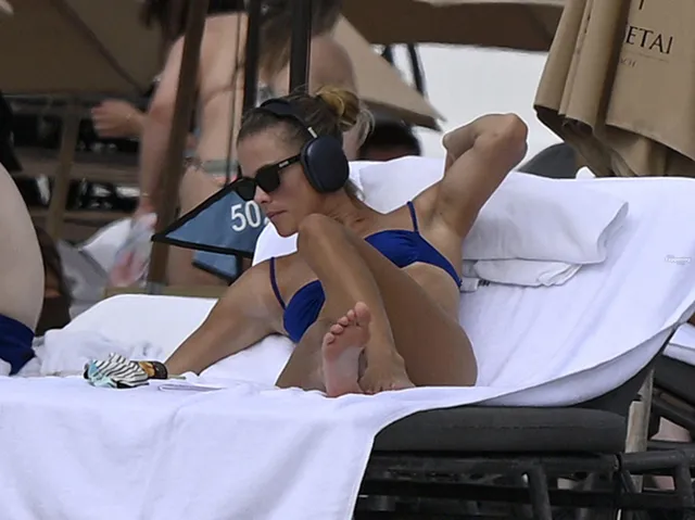Nina Agdal relaxing on a beach lounger in blue swimwear.