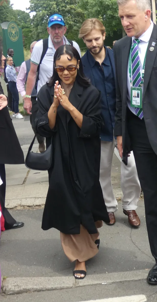 Tessa Thompson greeting guests in a dark long coat.