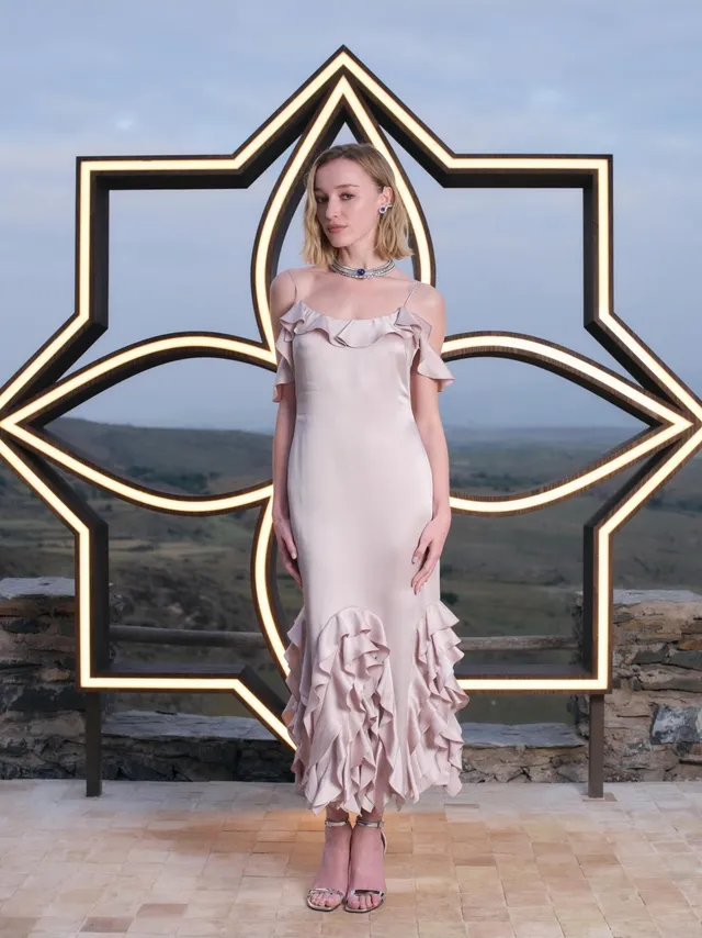 Phoebe Dynevor posing by the sea in a pale pink dress.