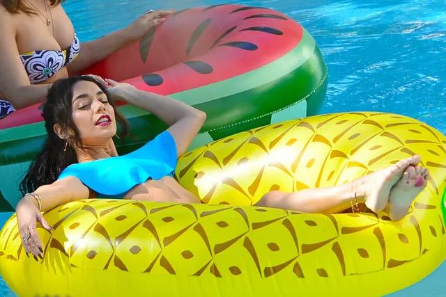 Vanessa Hudgens resting bare legs on a pool float beside another woman.