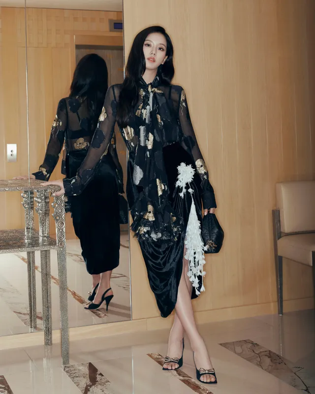 Jisoo wearing black heeled sandals and a dark patterned dress beside a mirror.