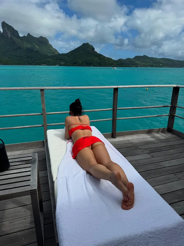 Demi Lovato lying on a lounger above turquoise water with bare soles visible.