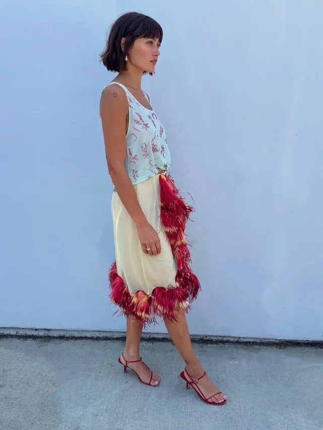 Ella Purnell posing outside in a feather trimmed skirt and sandals.