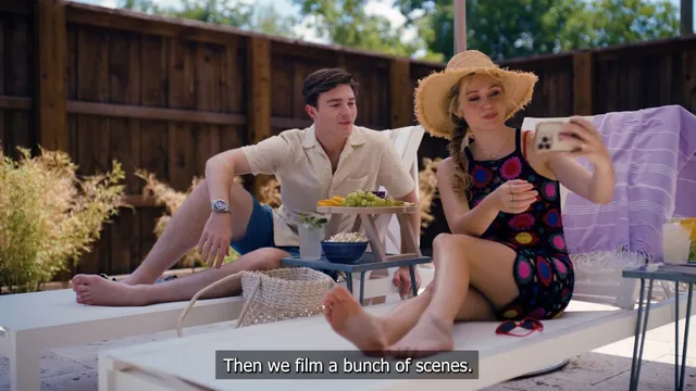 Brec Bassinger sitting barefoot beside a man on an outdoor sofa in a scene.